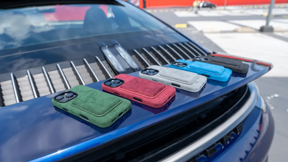 Zes kleurrijke smartphonehoesjes liggen op een blauwe autokap met een moderne achtergrond.