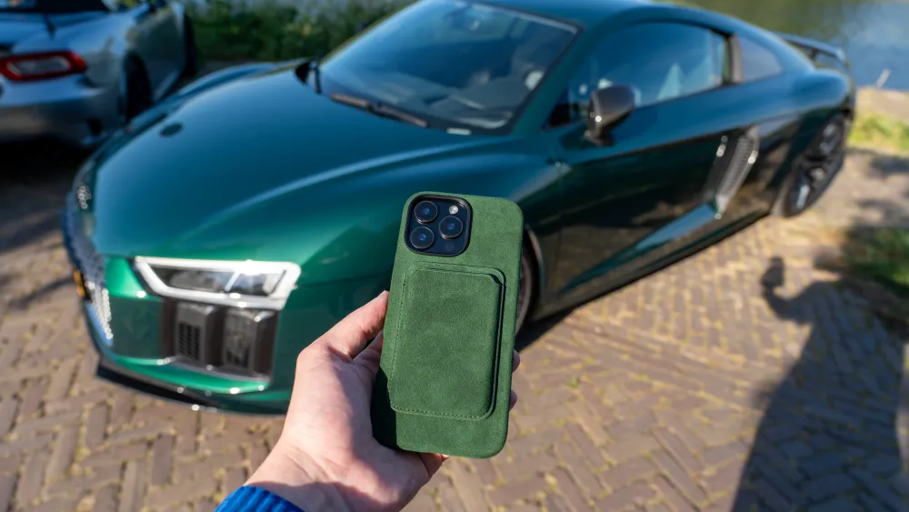 Hand houdt een groene telefoonhoes vast met een luxe groene sportauto op de achtergrond.