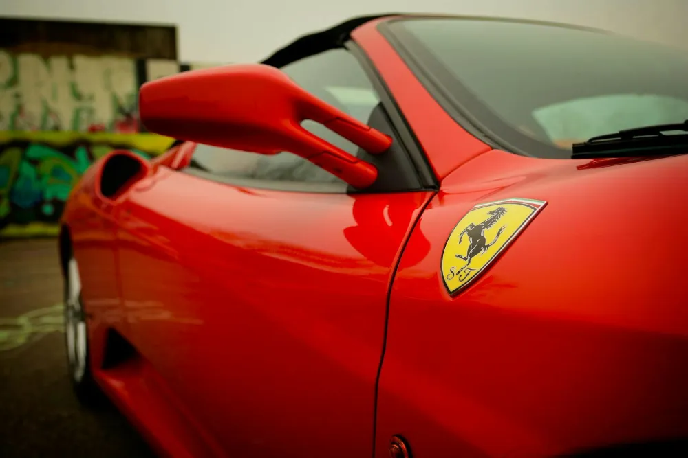 Rode sportauto met een Ferrari-logo op de zijkant, tegen een achtergrond van een graffiti-muur.