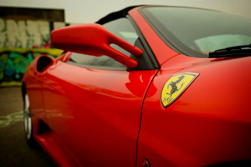 Rode sportauto met een Ferrari-logo op de zijkant, tegen een achtergrond van een graffiti-muur.