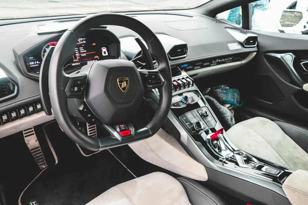 Stuurcabine van een luxe sportwagen met een lederen stuur, digitale dashboarddisplay en een moderne middenconsole met schakelaars en knoppen.